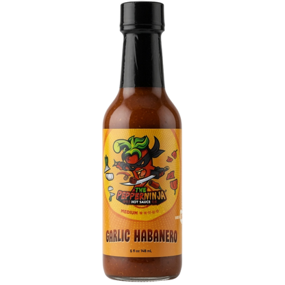 A bottle of The Pepperinja Garlic Habanero hot sauce on a plain white background. The bottle is filled with reddish-brown sauce, has a black cap, and a yellow label featuring a cartoon pepperinja character.