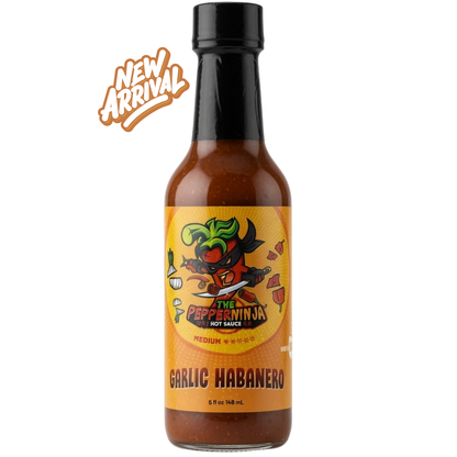 A bottle of Pepper Ninja Garlic Habanero hot sauce on a white background with a 'New Arrival' badge. The bottle contains a reddish-brown sauce and has an orange label with a cartoon ninja pepper character.