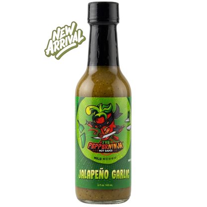 A bottle of Mild Hot Pepper Ninja Jalapeño Garlic hot sauce on a white background, featuring a green cartoon pepper graphic on the label and a 'NEW ARRIVAL' badge in the top left corner.